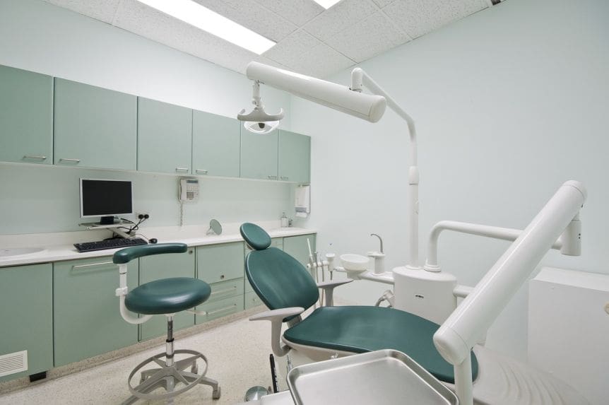 A dentist 's office with two green chairs and a desk.